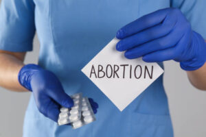 Doctor holding pills and paper card with word ABORTION